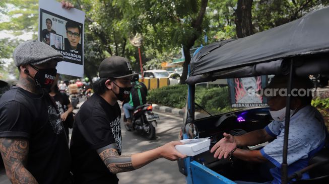 Penggemar musisi Jerinx SID dan band Superman Is Dead (SID), Outsider membagikan makanan dan masker kepada pengendara yang melintas saat menggelar aksi solidaritas di depan Pengadilan Negeri (PN) Jakarta Pusat, Jakarta, Selasa (22/2/2022). [Kabarindong.com/Angga Budhiyanto]