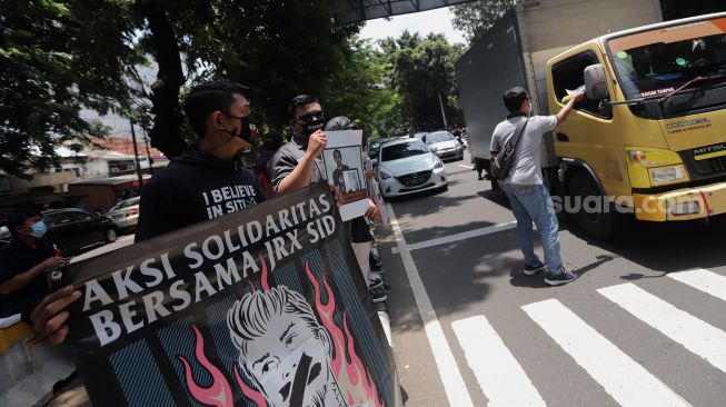 Penggemar musisi Jerinx SID dan band Superman Is Dead (SID), Outsider membagikan makanan dan masker kepada pengendara yang melintas saat menggelar aksi solidaritas di depan Pengadilan Negeri (PN) Jakarta Pusat, Jakarta, Selasa (22/2/2022). [Kabarindong.com/Angga Budhiyanto]