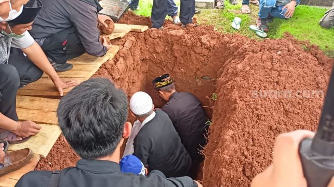 Doddy Sudrajat turun hingga ke liang lahad memakamkan jenazah ayahnya, di TPU Malaka, Pondok Kopi, Jakarta Timur, Jumat (18/2/2022). [Rena Pangesti/Kabarindong.com]